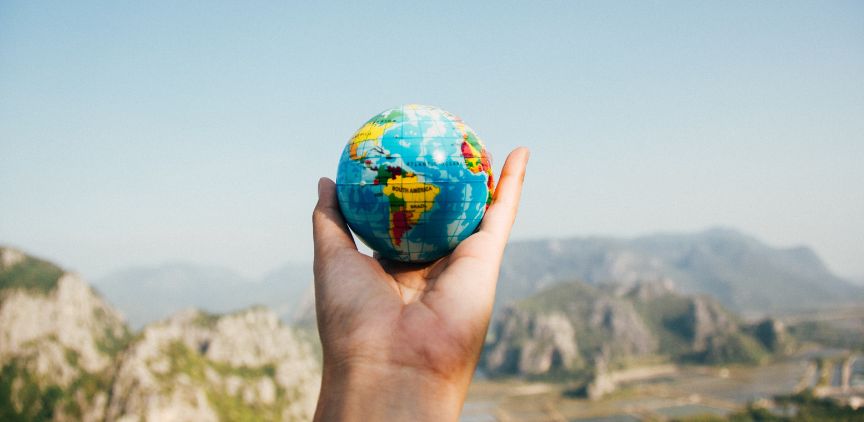 A hand holding up a small model of a globe.