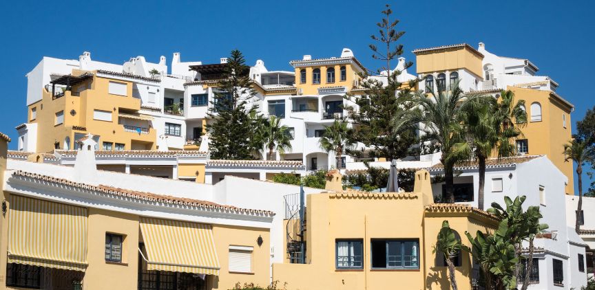 Yellow and white buildings along a hillside, with trees in between them.