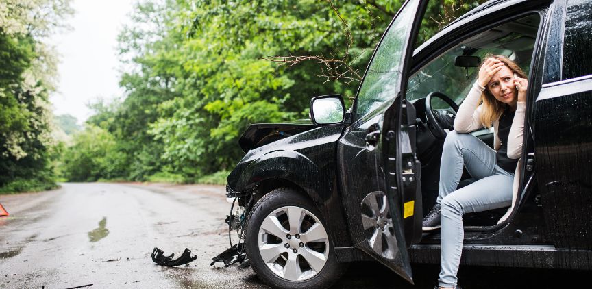 A woman sitting in an SUV with the door open, after a car accident. She is on her phone, looking upset.