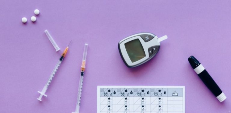 Insulin shots, a blood sugar monitor, and white pills on a purple background.