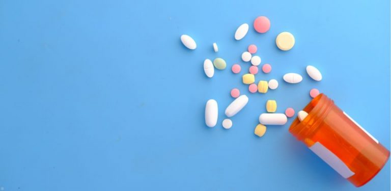 An assortment of pills being poured from an orange pill bottle on a blue background.