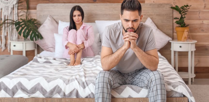 A couple sitting in bed together. They look disappointed and frustrated.