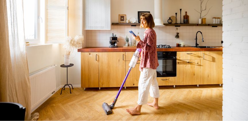 A woman vacuuming her house with a cordless vacuum.