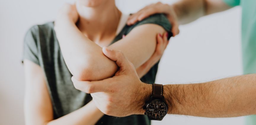 A woman stretching her arm with help from a physical therapist.