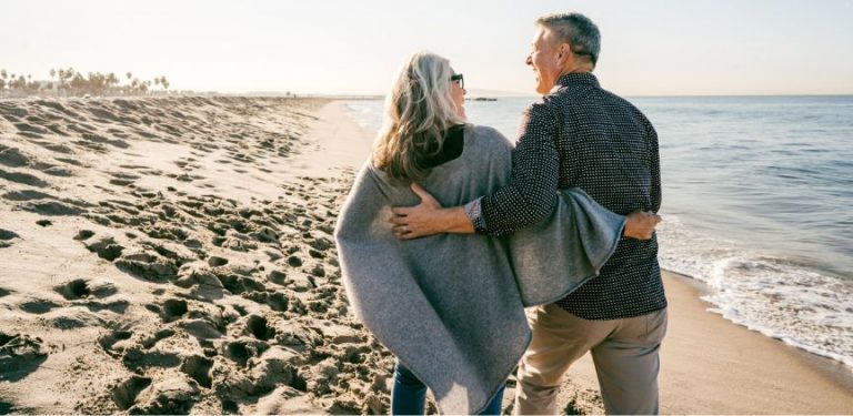 An older couple walking together on a beach.