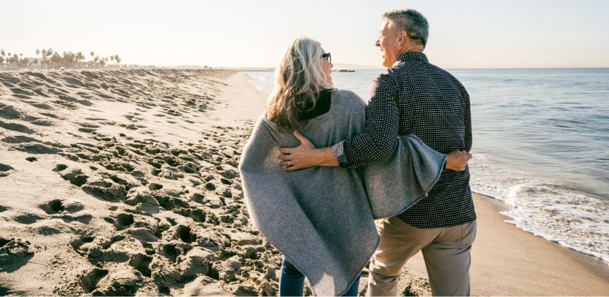 An older couple walking together on a beach.