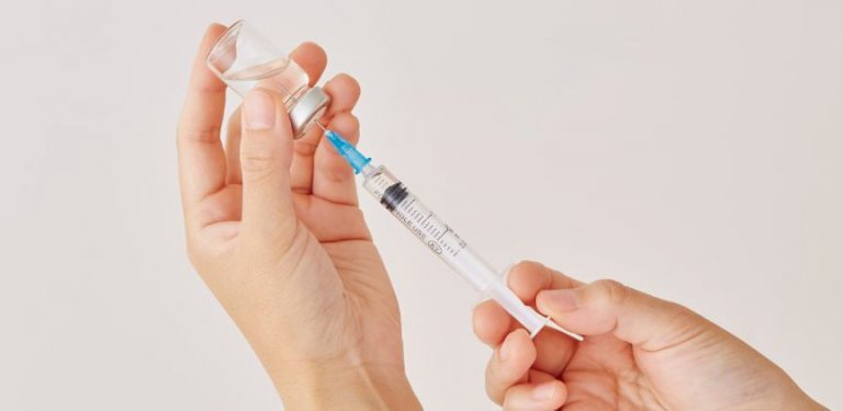 Two hands filling a medical needle with a liquid injection treatment.