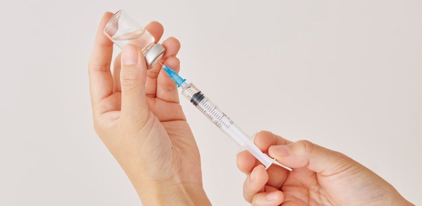 Two hands filling a medical needle with a liquid injection treatment.