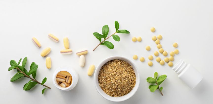 An assortment of vitamins on a white surface with some plant leaves.